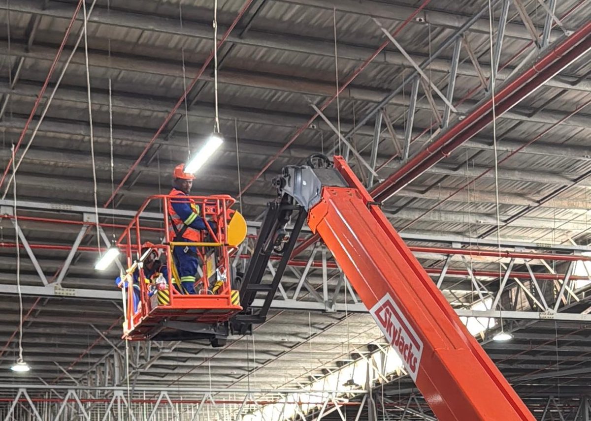 Electrician replacing warehouse ceiling lights from a boom lift